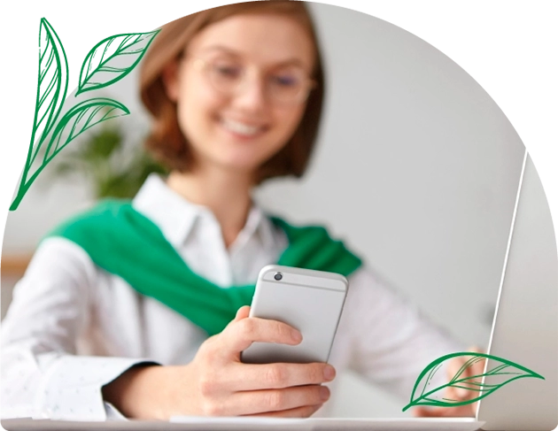 Kobieta w białej koszuli i zielonym swetrze na ramionach, uśmiecha się, patrząc na smartfon - terapie naturalne szczecin